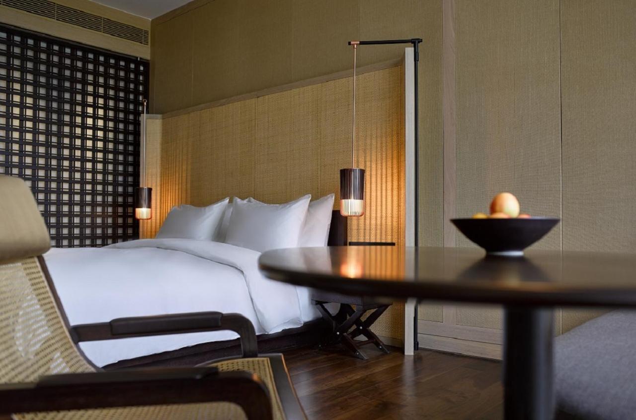 The Ruma Hotel And Residences Kuala Lumpur Exterior photo The photo shows a well-designed bedroom with a modern and minimalist aesthetic. The room features a large bed with white linens, positioned against a textured wall. On either side of the bed, there are pendant lights that provide a warm glow. The dec