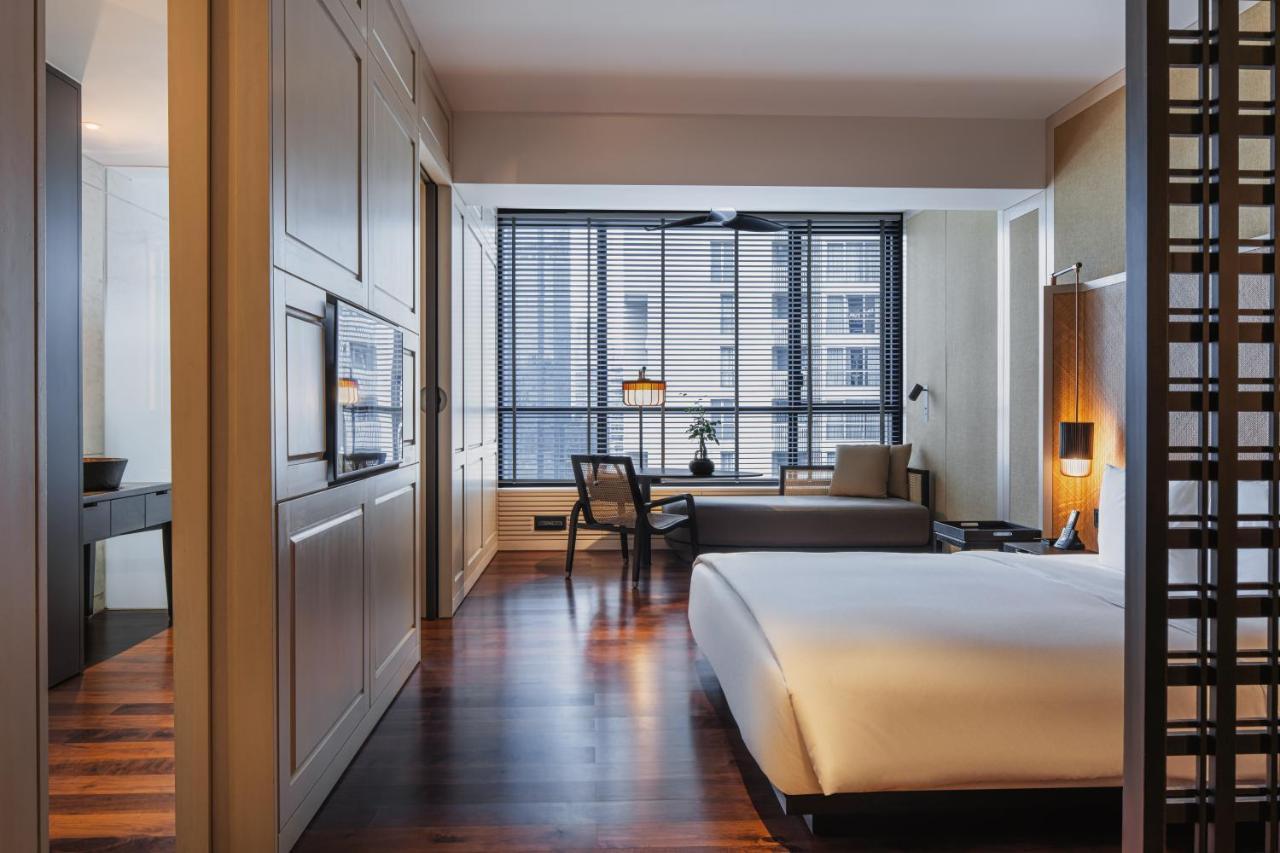 The Ruma Hotel And Residences Kuala Lumpur Exterior photo The photo shows a modern hotel room with a clean and minimalist design. The room features a large bed with white bedding positioned against a wall. There is a wooden floor that adds warmth to the space. A sitting area is visible in the background, fe