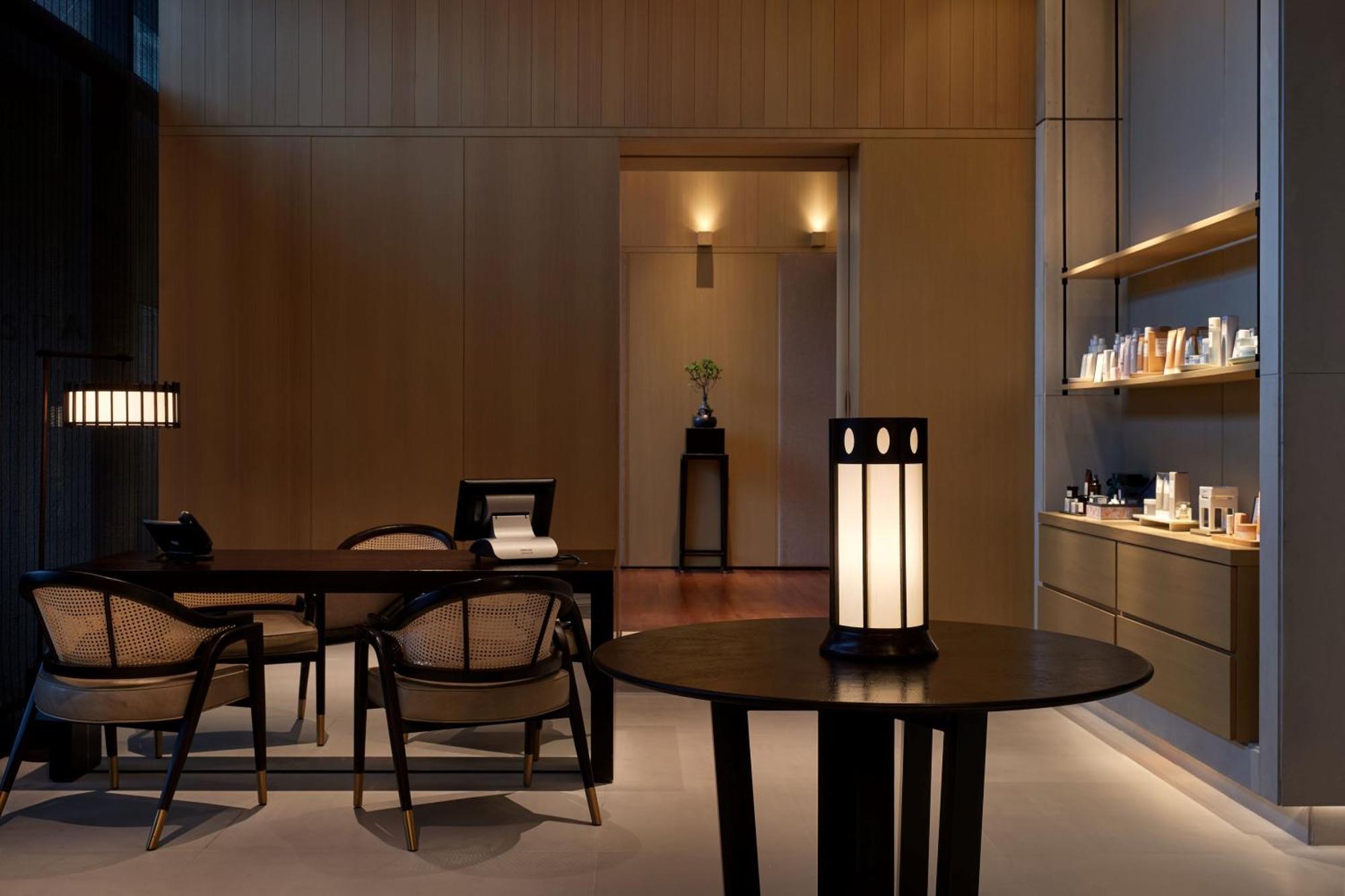 The Ruma Hotel And Residences Kuala Lumpur Exterior photo The photo shows a modern, minimalist interior space. It features a wooden wall with soft lighting, enhancing a calm atmosphere. In the foreground, there is a round table with a uniquely designed lamp on it. Surrounding the table, there are stylish wo